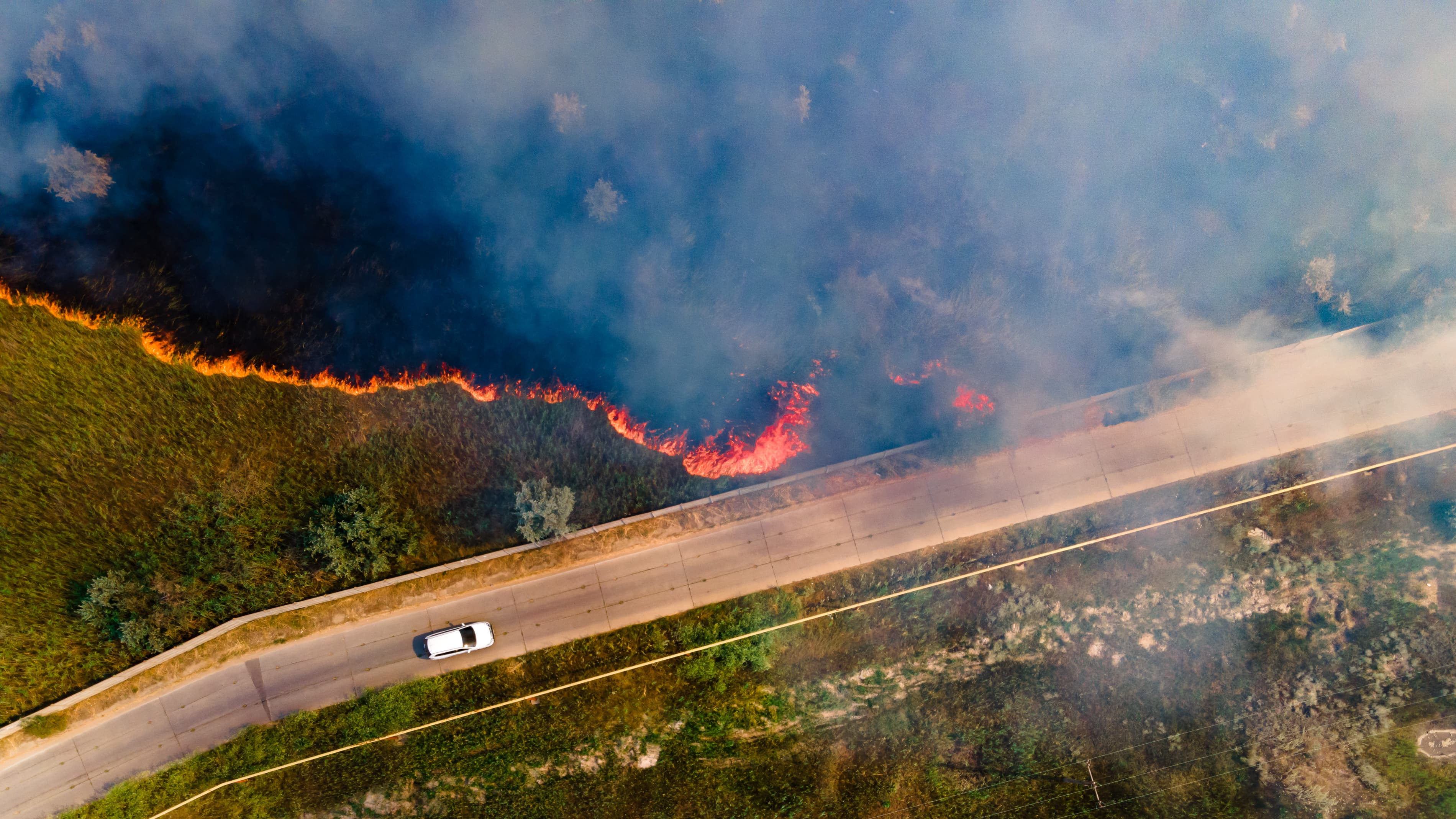 Aerial view of a bushfire burning beside a road with smoke drifting across the landscape