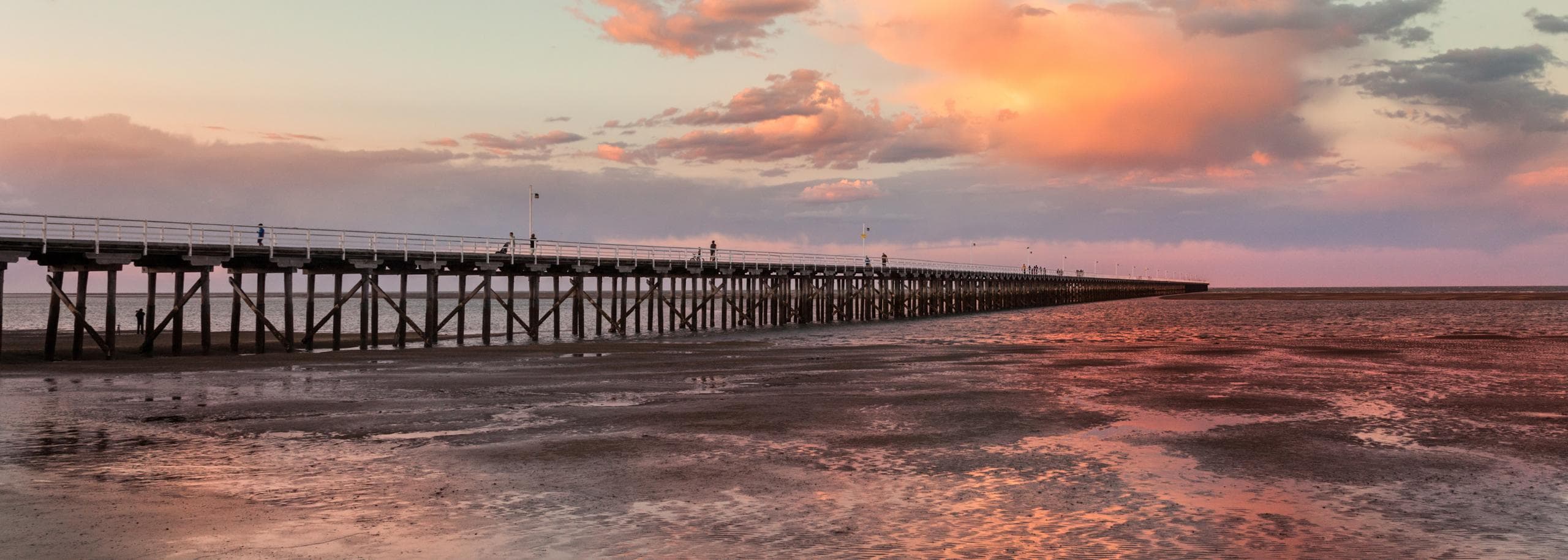 Wooden pier stretching over tidal flats at sunset in Queensland